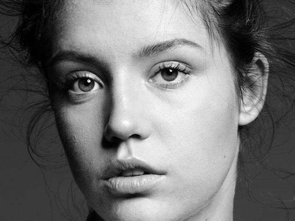 Obrázok zachytáva Adèle Exarchopoulos, francúzsku herečku, známu svojimi emotívnymi a silnými hereckými výkonmi. Na tomto zábere je Adèle zachytená v čiernobielej fotografii, kde jej výrazná, no prirodzená krása vyžaruje silu a eleganciu. Je oblečená v jednoduchom, ale sofistikovanom oblečení, ktoré zdôrazňuje jej osobitý štýl. Jej tmavé vlasy sú voľne prehodené cez plece a jej pohľad je priamy, s jemným náznakom úvah. Tento výraz evokuje intenzitu a hĺbku, ktoré sú charakteristické pre jej hereckú prácu. Okolité svetlo vytvára jemné tiene, ktoré zdôrazňujú jej tvár, pričom zachytáva jej silnú osobnosť a záhadný šarm. Celková atmosféra obrázku odráža Adèlinu schopnosť zanechať nezmazateľný dojem v každom projekte, na ktorom sa podieľa. Tento záber zobrazuje nielen jej krásu, ale aj jej umenie v prenose emócií prostredníctvom kamery.