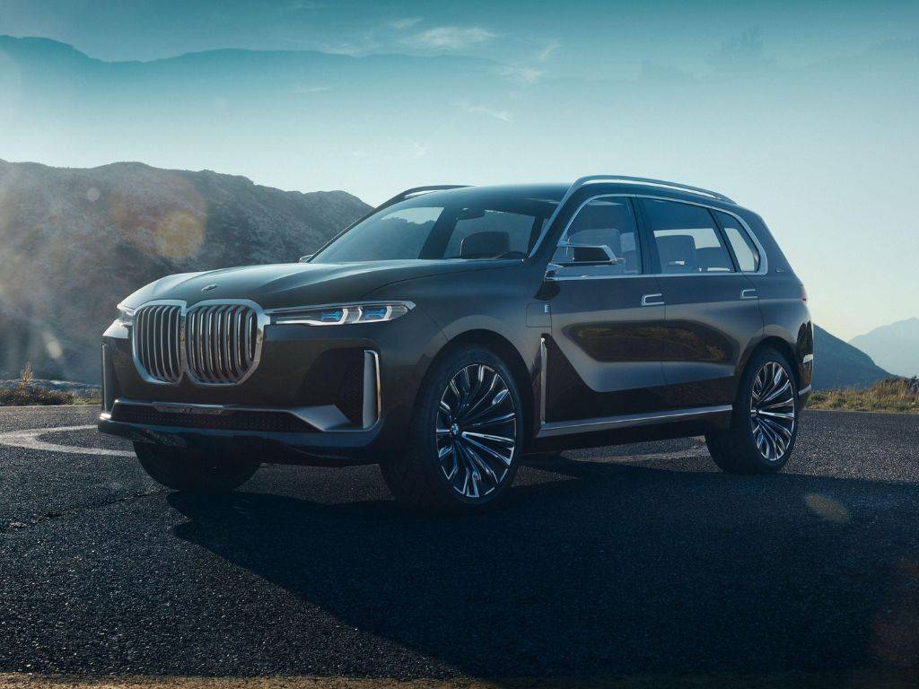 Obrázok zobrazuje elegantný a impozantný BMW X7, luxusný SUV, ktorý kombinuje špičkový výkon a štýlový dizajn. Na zábere je vozidlo zachytené v exteriéri, kde vyniká jeho robustná a sofistikovaná silueta. Predná časť je dominovaná výraznou mriežkou chladiča, ktorá je typická pre modely BMW, a LED svetlami, ktoré dodávajú autu moderný a agresívny vzhľad. Farba karosérie je tmavá a lesklá, čo podčiarkuje jeho luxusný charakter. Okolo neho sa nachádza elegantné prostredie, ktoré zdôrazňuje jeho prítomnosť na ceste. Kolesá sú veľké a štýlové, čo podčiarkuje jeho schopnosti v teréne aj na diaľnici. Interiér BMW X7 je viditeľný cez otvorené okná a ponúka náznak komfortu a prémiových materiálov. Tento obrázok perfektne zachytáva BMW X7 ako symbol luxusu, výkonu a pokročilých technológií v jednom nádhernom balíku.