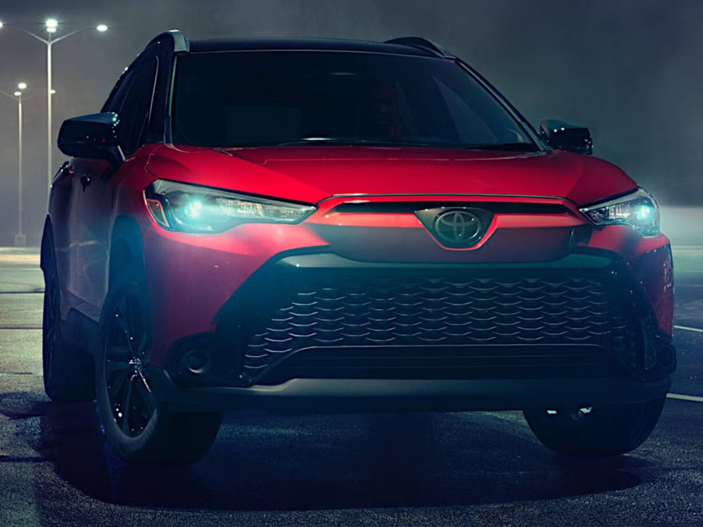 Na obrázku je zachytená Toyota Corolla Cross Hybrid z roku 2024, elegantné a praktické SUV, ktoré spája spoľahlivosť s modernými technológiami. Vozidlo vyniká svojou robustnou, no zároveň aerodynamickou siluetou, ktorá ponúka ideálnu kombináciu mestského štýlu a off-road schopností. Predná časť dominuje štýlovou mriežkou chladiča a dynamickými LED svetlami, ktoré pridávajú vozidlu moderný vzhľad. Karoséria je vyhotovená vo svetlom metalickom odtieni, ktorý zdôrazňuje jemné línie a čistý dizajn. Veľké kolesá s elegantnými diskami podčiarkujú jeho terénne schopnosti a robustnosť. Na pozadí je vidieť mestské prostredie, ktoré naznačuje, že ide o ideálne vozidlo pre každodenné použitie aj dlhšie výlety. Hybridná technológia Toyota je nenápadne integrovaná, pričom ponúka tichú a efektívnu jazdu s nízkou spotrebou paliva. Tento obrázok vystihuje Toyota Corolla Cross Hybrid ako moderné SUV, ktoré prináša štýl, komfort a inovatívnu technológiu pre každého vodiča.